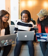 three women sitting on sofa with MacBook