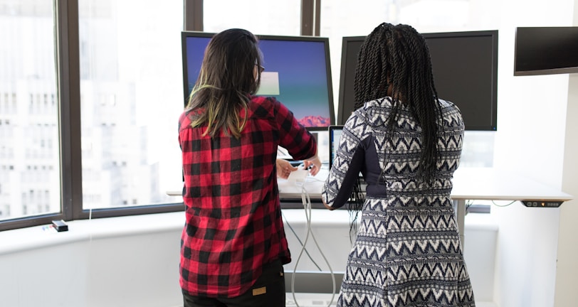 two women standing in front of two black monitors