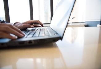 person using black laptop on brown table